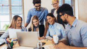 A diverse group of employees gathered around a laptop in a bright office, symbolising collaboration and the benefits of workplace mortgage advice clinics