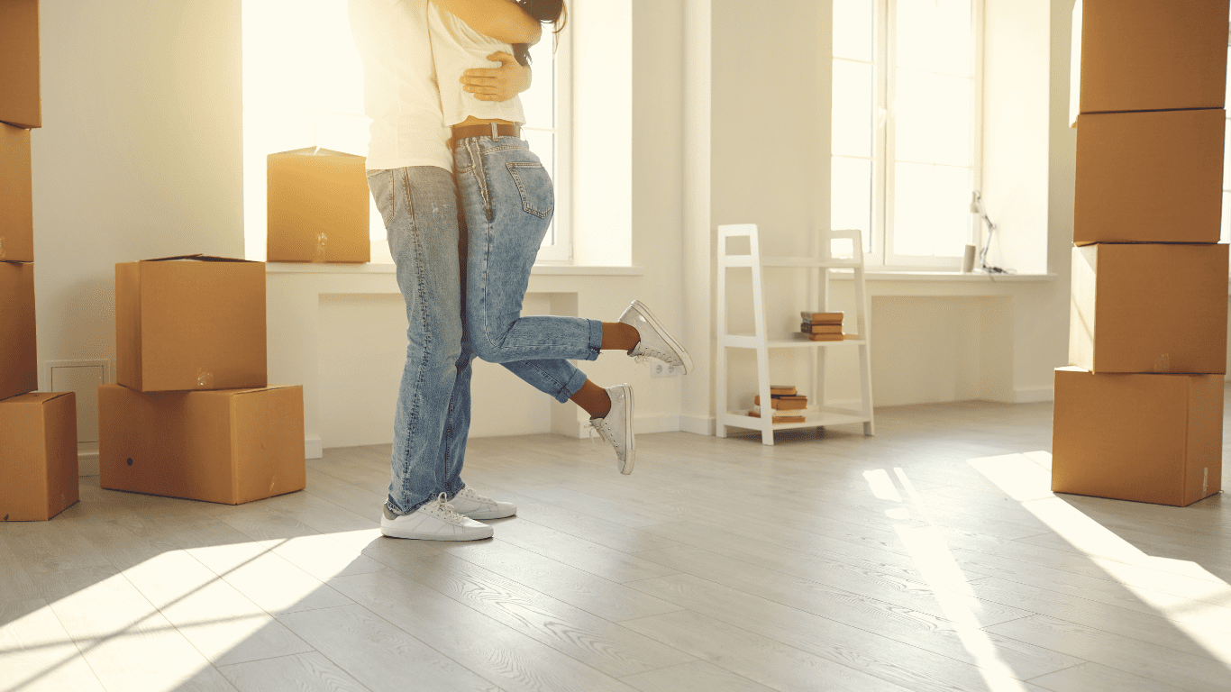 Interest-only mortgage explained: A happy couple embraces in their new home, surrounded by moving boxes, symbolising homeownership with flexible mortgage repayment options