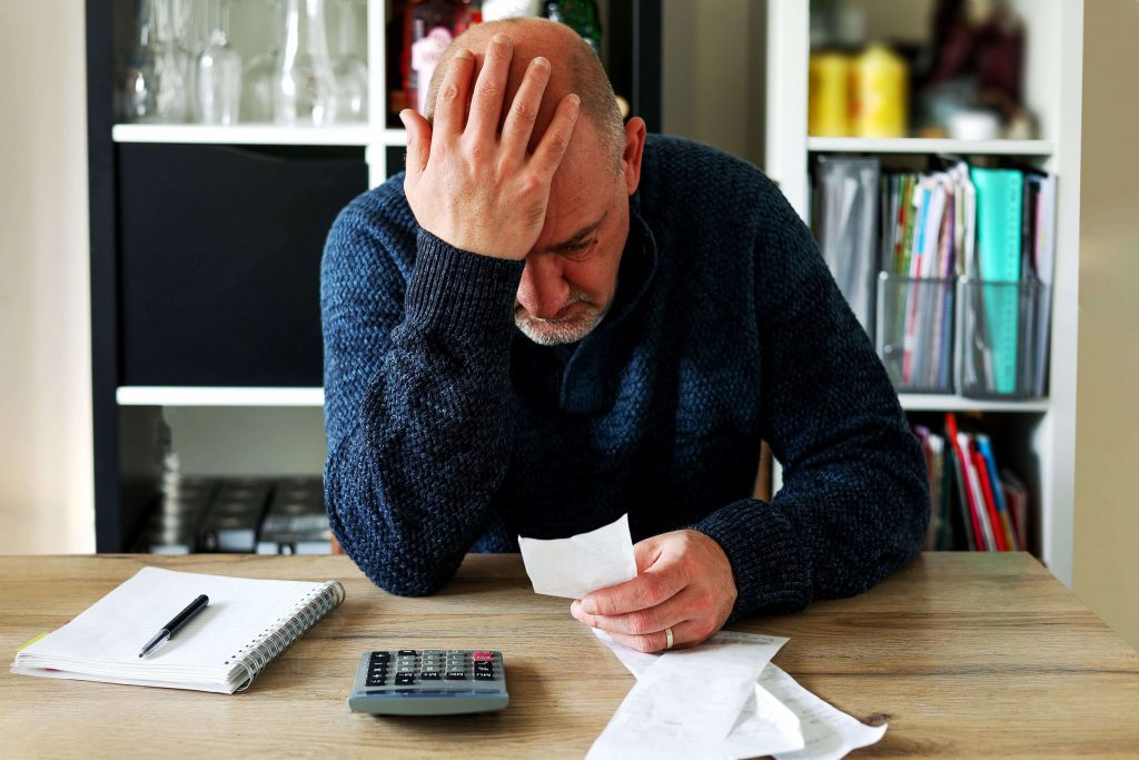 Man sat at his kitchen table, with a stressed out look on his face, during the cost of living crisis, looking at receipts because his monthly outgoings have gone up significantly.