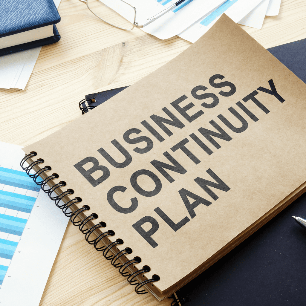 Open notebook titled 'Business Continuity Plan' on a desk with documents and charts, representing strategic planning for business stability