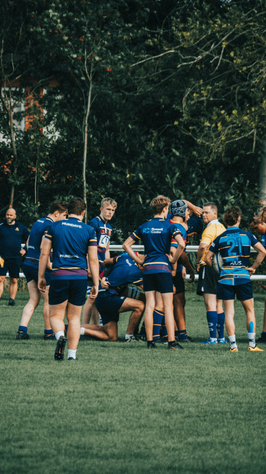 A group of rugby players huddled on the field, with one player crouching, possibly injured, and others standing around, highlighting the importance of sports injury insurance