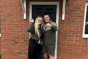 New homeowners holding house keys outside their property after mortgage