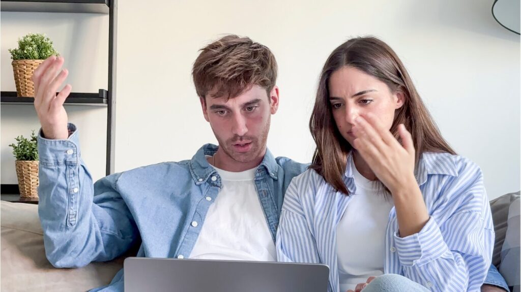 Young first-time buyer couple discussing guarantor mortgage options and affordability challenges while reviewing information on a laptop.